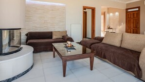 A living room with a brown sofa, a glass coffee table, and a white tiled floor. - Sea and City Views Apartment in Villa Zina (Rethymno)