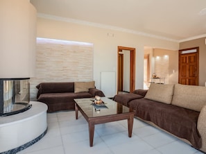 A living room with a brown sofa, a glass coffee table, and a white tiled floor. - Sea and City Views Apartment in Villa Zina (Rethymno)