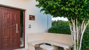 A villa entrance with a wooden door, a bench, a small table, and a sign on the wall. - Sea and City Views Apartment in Villa Zina (Rethymno)