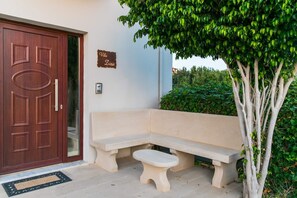 A villa entrance with a wooden door, a bench, a small table, and a sign on the wall. - Sea and City Views Apartment in Villa Zina (Rethymno)