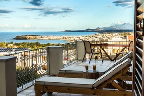 Ein Balkon mit Blick auf das Meer und die Berge, eine Liege und ein Tisch mit Getränken.