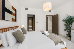 Ein Hotelzimmer mit einem großen Bett, einem hölzernen Kopfteil, einem an der Wand befestigten Kunstwerk, einer Topfpflanze und einer Tür zu einem weiteren Raum.