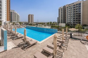 Ein Dachpool mit Liegestühlen und Sonnenschirmen, umgeben von Hochhäusern.