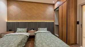 A bedroom with two beds, a herringbone-patterned wall, a wooden wardrobe, and a mirror. - Spacious 3 Bedroom Apartment in Tangier - Near Stadium, Airport and Beaches (Tanger)