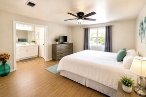 Un dormitorio con cama, cómoda, televisor, ventilador de techo y ventana con cortinas.