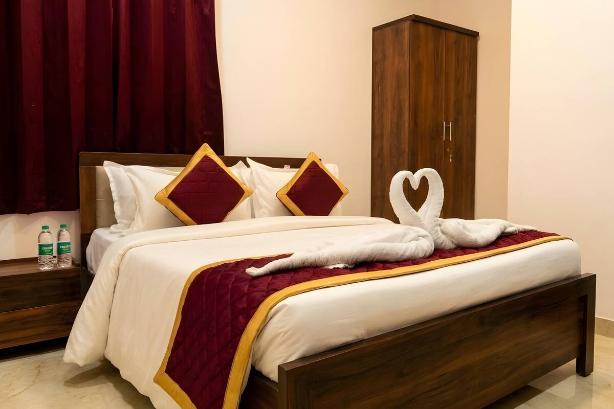 Un lit bien fait, recouvert d’une couvre-lit rouge et or, avec deux oreillers ornés de bordures rouges et dorées, et une serviette pliée en forme de cygne.