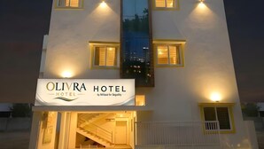 A hotel with a central vertical glass feature, multiple windows with yellow trim, and a sign reading 'OLIVRA HOTEL by Milase for Segility.'