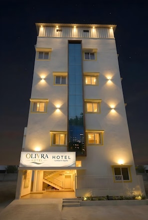 A hotel with a central vertical glass feature, multiple windows with yellow trim, and a sign reading 'OLIVRA HOTEL by Milase for Segility.' - Olivra Hotel By Welcome Inn Hospitality (Bengaluru)