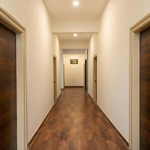 A hallway with wooden flooring, white walls, and doors on both sides. - Olivra Hotel By Welcome Inn Hospitality (Bengaluru)