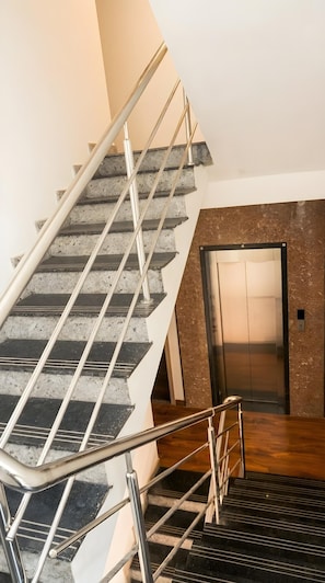 A staircase with metal railings leading to an elevator. - Olivra Hotel By Welcome Inn Hospitality (Bengaluru)