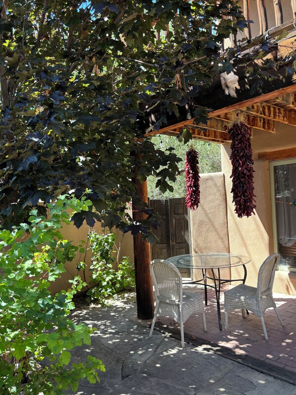 A patio with a glass table and wicker chairs, surrounded by greenery and a wooden pergola. - Casa de Monte Vista, balcony, patios, 3/3, 2 kit, 3 lvg areas, walk to Canyon Rd (Santa Fe)