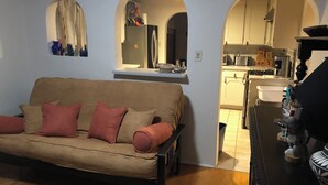 Ein Wohnzimmer mit einer Couch, einer Küchenzeile inklusive Geräte und einem Esstisch.
