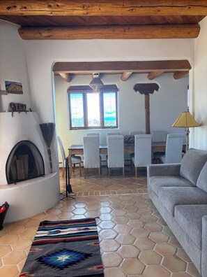 A living room with a fireplace, a sofa, a patterned rug, and a dining area with chairs and a table. - Casa de Monte Vista, balcony, patios, 3/3, 2 kit, 3 lvg areas, walk to Canyon Rd (Santa Fe)