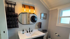 Une salle de bain avec un lavabo blanc, des meubles sombres, un miroir rond et des toilettes.