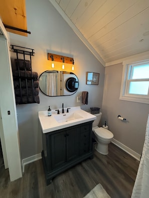 A bathroom with a white sink, dark cabinets, a round mirror, and a toilet.
