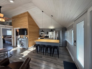 A modern kitchen with a wooden accent wall, stainless steel appliances, and a bar area with stools.