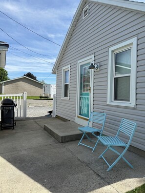 A house with a porch, two blue chairs, a grill, and a white fence.