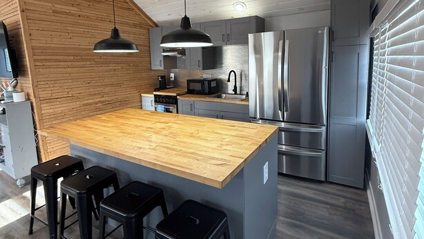 Une cuisine moderne dotée d’un îlot central en bois, de tabourets de bar, d’appareils électroménagers en acier inoxydable et d’un plafond en pente.