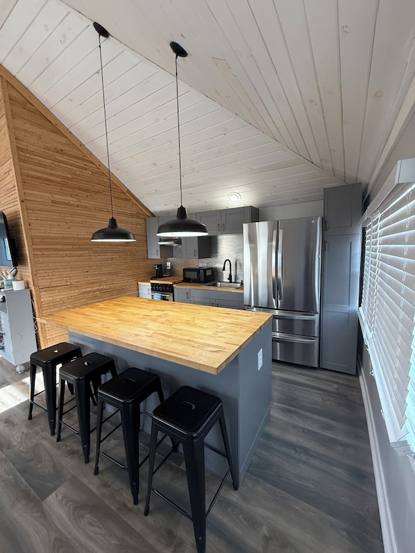 A modern kitchen with a wooden island, bar stools, stainless steel appliances, and a sloped ceiling.