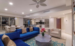 Una sala de estar moderna con un sofá azul, un sillón beige, una mesa de centro y un comedor con mesa y sillas.