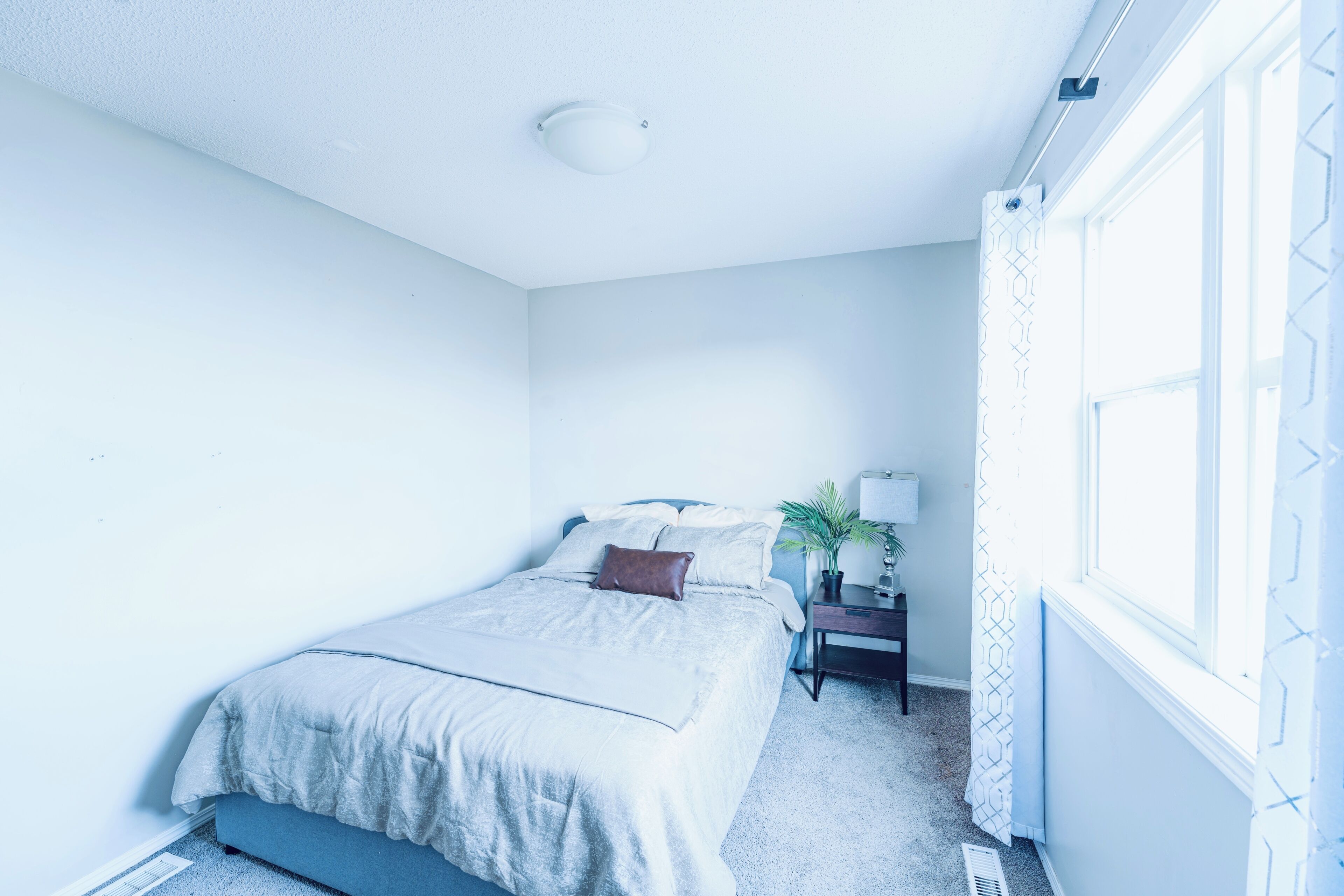 Une chambre à coucher avec un lit, une table de chevet, une lampe et une fenêtre avec des rideaux.