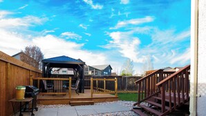 Un jardin avec une terrasse en bois, un barbecue et un espace patio couvert.