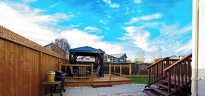 Un jardin avec une terrasse en bois, un barbecue et un espace patio couvert.