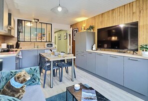 Eine moderne Küche mit grauen Schränken, einem großen Fernseher und einem Essbereich mit Tisch und Stühlen.