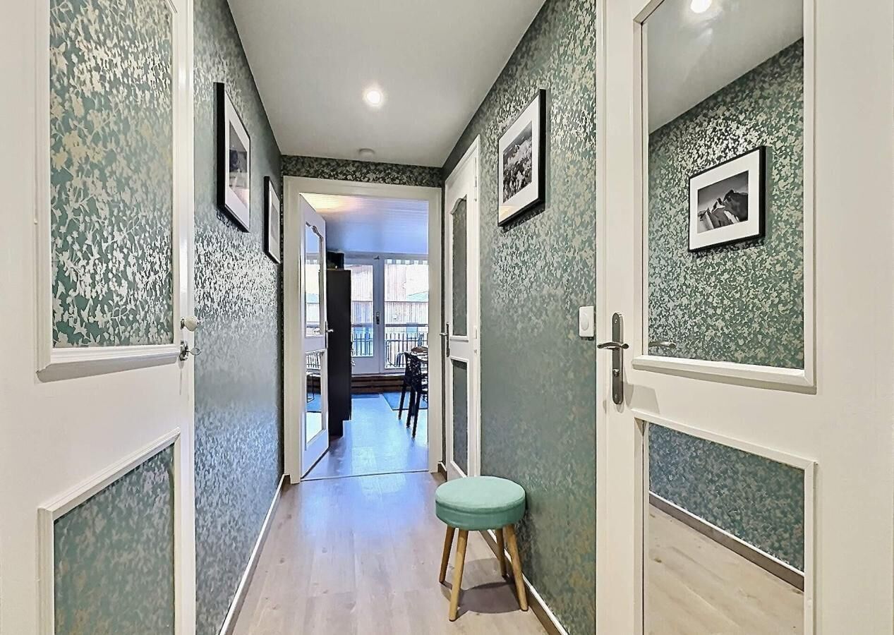 A hallway with patterned walls, a green stool, and framed pictures.