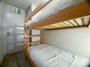 Ein Etagenbett mit weißer Matratze, Holzrahmen und einer weißen Tür.