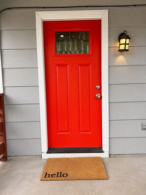 A red door with a glass panel, a doormat with 'hello' written on it, and a wall-mounted light fixture. - Pet-Friendly Central Austin Bungalow - Near Hospitals, Tech Corridor & Downtown (Austin)