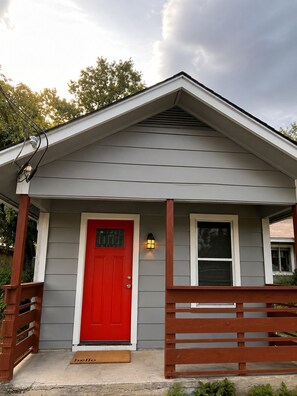 Une maison avec une porte rouge, un petit porche et une clôture en bois.