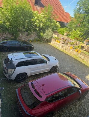 A parking area with three cars, a stone wall, and greenery.