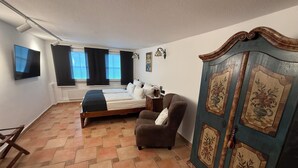 Un dormitorio con cama, una silla, armario, televisión y ventana con cortinas.