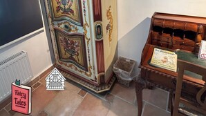 Een kast in vintage-stijl met decoratieve bloemmotieven, een klein houten tafeltje met een boek, en een radiator op de vloer.