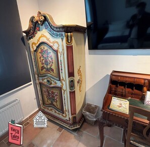 A vintage-style cabinet with ornate floral designs, a small wooden table with a book, and a radiator on the floor. - Grebenstein with castle & towers near Sleeping Beauty's Sababurg & Rapunzel's Trendelburg (Grebenstein)