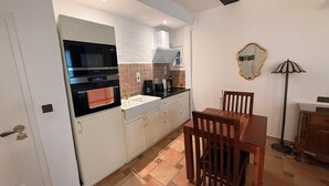Een kleine keuken met witte kastjes, een zwarte magnetron, een spoelbak en een eettafel met stoelen.