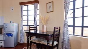Ein Essbereich mit Tisch, Stühlen, einem Kühlschrank und einem fensterbepflanzten Fenster.