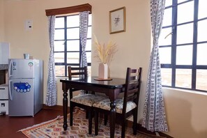 Un comedor con una mesa, sillas, refrigerador y una ventana con cortinas.