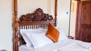 Ein Bett mit Baldachin, dessen Kopfteil aus geschnitztem Holz gefertigt ist, mit weißen Leinen und einem orangefarbenen Kissen.