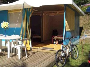 Una tienda de campaña con una mesa y sillas afuera, una bicicleta y una pequeña mesa con objetos encima.