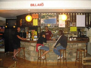 Un bar con taburetes, una barra y un letrero que dice 'BILLARD'.