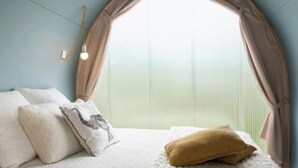 Una camera da letto con un letto, cuscini, una finestra con tende e un lampadario a parete.