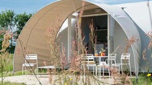 Una tenda a forma di cupola con l'ingresso aperto, un tavolo con sedie e vista sul paesaggio circostante.