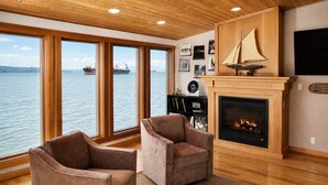 Ein Zimmer mit Kamin, zwei Sesseln, einem Fernseher und Meerblick.
