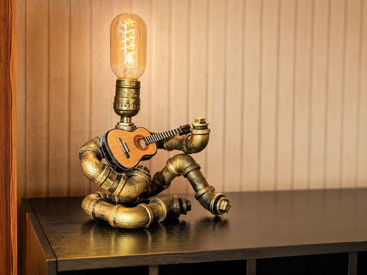 Un robot avec une guitare et une tête en forme d’ampoule, assis sur une table.