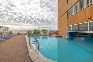 Una piscina amb vistes a l'oceà, una zona coberta amb gandules i un edifici amb grans finestrals.