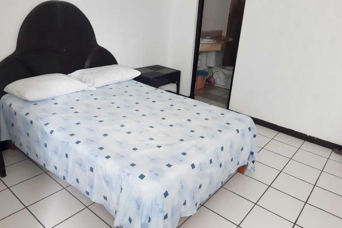 A bedroom with a bed, two pillows, a nightstand, and a mirror.