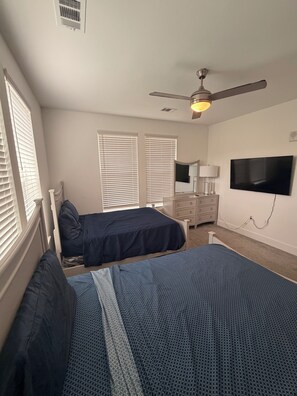 Ein Schlafzimmer mit zwei Betten, einem Deckenventilator, einem Fernseher und einer Kommode.