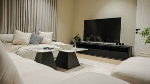 A modern living room with a sofa, two coffee tables, a flat-screen TV, and a potted plant. - 5 mins to the sea ~1BR luxury apartment ~Pool ~ Fast Wi-Fi (Al Khobar)